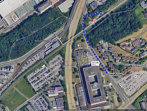 Der Fussweg Hardacher–Balsberg (blau) zieht sich. Nun soll die Haltestelle auch von Opfiker Seite besser erschlossen werden. Unten in der Mitte der ehemalige Swissair-Hauptsitz, links daneben die Flughafenautobahn, diagonal übers Bild die Bahnlinie (Zürich-)Opfikon-Kloten(-Winterthur) und daneben nach oben abzweigend die Glattalbahn. Illustration: Google Maps