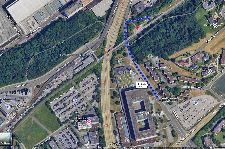 Der Fussweg Hardacher–Balsberg (blau) zieht sich. Nun soll die Haltestelle auch von Opfiker Seite besser erschlossen werden. Unten in der Mitte der ehemalige Swissair-Hauptsitz, links daneben die Flughafenautobahn, diagonal übers Bild die Bahnlinie (Zürich-)Opfikon-Kloten(-Winterthur) und daneben nach oben abzweigend die Glattalbahn. Illustration: Google Maps