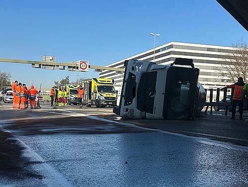 Im Schatten der Brücke liegt der Betontransporter auf seiner linken Seite, im Vordergrund verteilt sich Diesel auf der Strasse. Im Hintergrund vor einem strahlend blauen Himmel ist der ehemalige «Swissair»-Hauptsitz Balsberg zu sehen. 