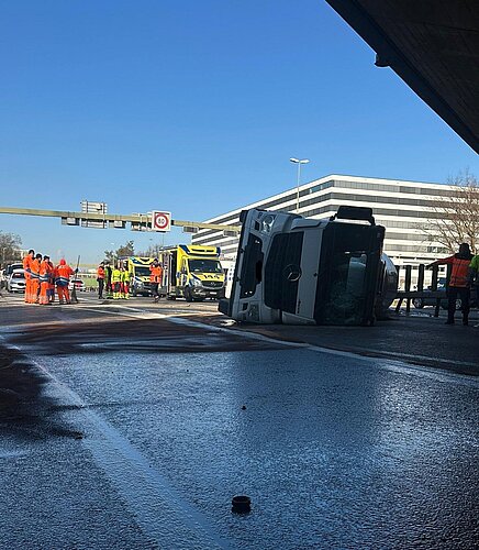 Im Schatten der Brücke liegt der Betontransporter auf seiner linken Seite, im Vordergrund verteilt sich Diesel auf der Strasse. Im Hintergrund vor einem strahlend blauen Himmel ist der ehemalige «Swissair»-Hauptsitz Balsberg zu sehen. 